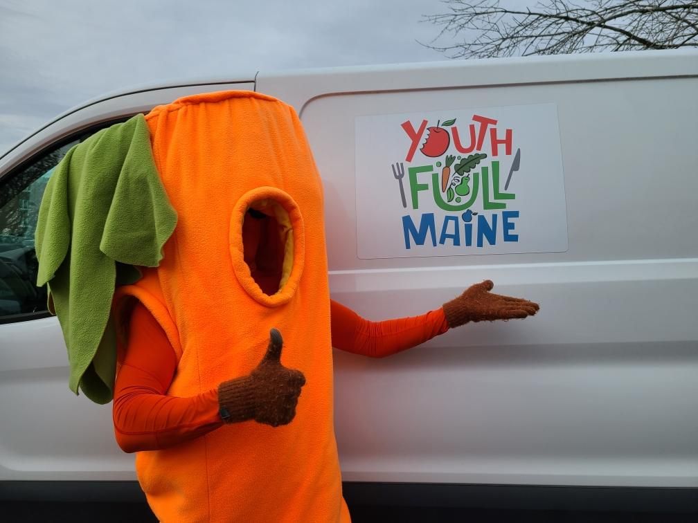 Youth Full Maine human-sized Carrot mascot showing Youth Full Maine Logo on white work van